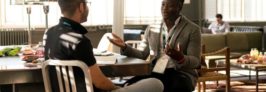Two men sitting at a table with notebooks, engaged in discussion