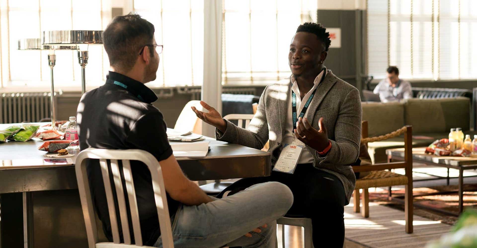 Two men sitting at a table with notebooks, engaged in discussion