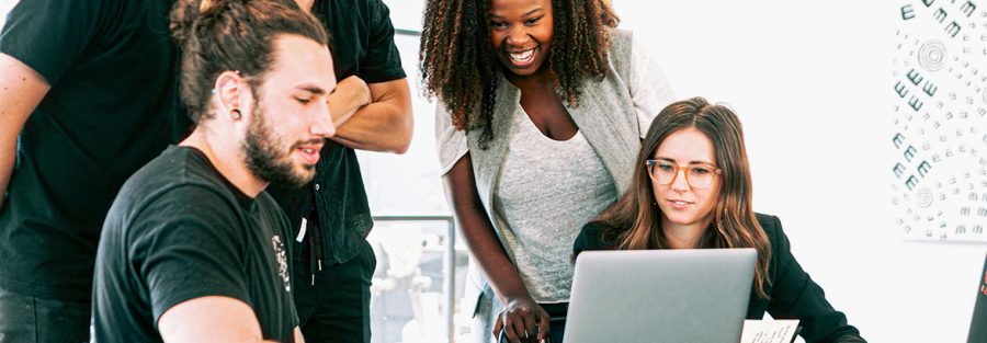 Group of people gathered around a laptop, laughing