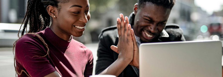 Man and woman using a laptop, smiling and giving a high five